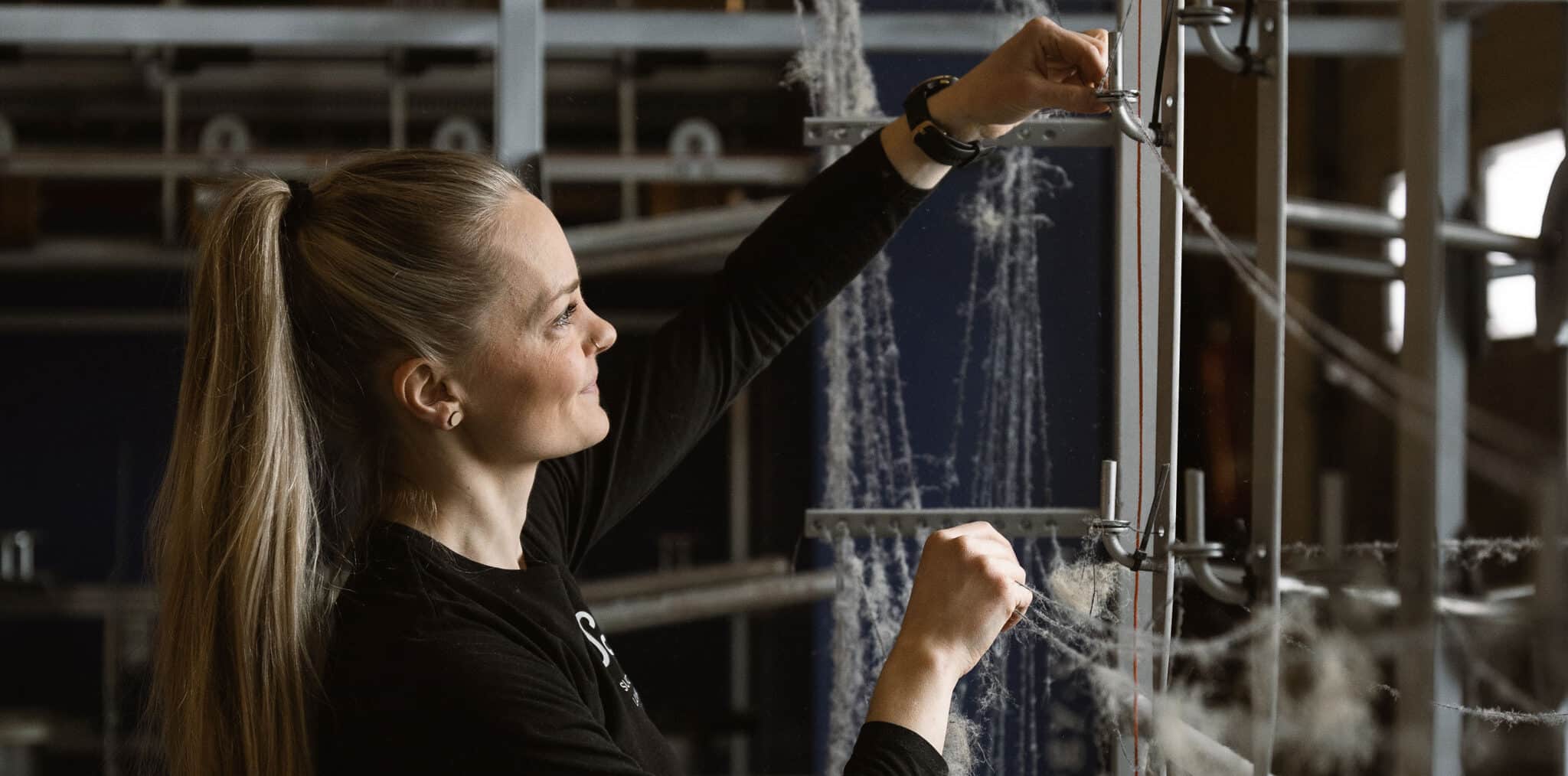 Työntekijä säätää lankoja tuotannossa, kuvastaen että Suomen Langan valmistusprosessi on kotimainen ja vastuullinen.