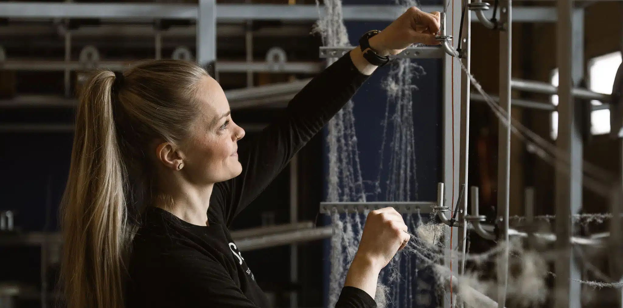 Työntekijä säätää lankoja tuotannossa, kuvastaen että Suomen Langan valmistusprosessi on kotimainen ja vastuullinen.