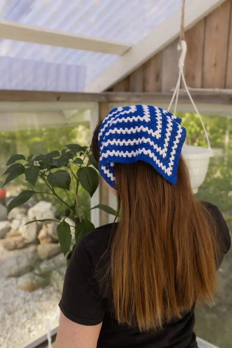 Hilkka-bandana sinivalkoisena päähineenä kasvihuoneessa puutarhaa hoitavalla naisella.