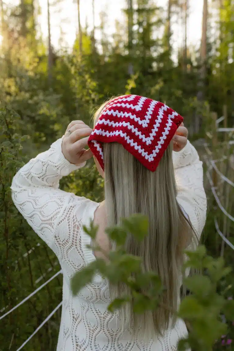 Punavalkoinen Hilkka-bandana ja luonnonvalkoinen palmikkoneule metsässä.