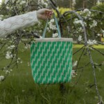 Molla Millsin Viive-laukku roikkuu kukkivan puun oksalla puutarhassa.