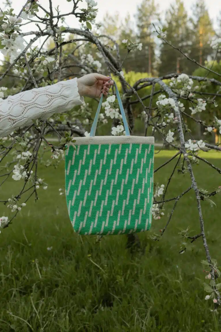Molla Millsin Viive-laukku roikkuu kukkivan puun oksalla puutarhassa.